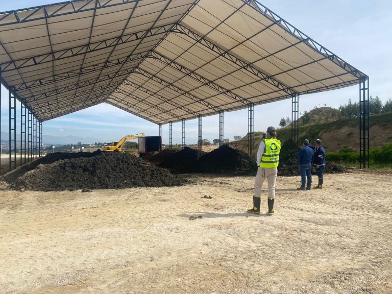 Personal junto a pilas de material orgánico en un área cubierta de compostaje.